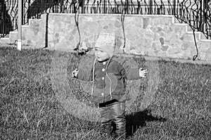 Little baby girl in jeans jacket and hat making learning to walk his first steps on the lawn in the green grass