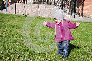 Little baby girl in jeans jacket and hat making learning to walk his first steps on the lawn in the green grass