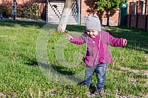 Little baby girl in jeans jacket and hat making learning to walk his first steps on the lawn in the green grass