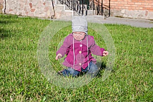 Little baby girl in jeans jacket and hat making learning to walk his first steps on the lawn in the green grass it has not very go