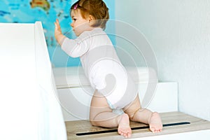 Little baby girl learning walking, standing and making first steps at home. Toddler climbing stairs and balancing. Happy