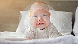 Little baby girl lies on belly on parent bed and smiles