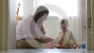 Little baby girl and mommy play with colorful toys at home sitting on floor. Mother and daughter laughing having fun