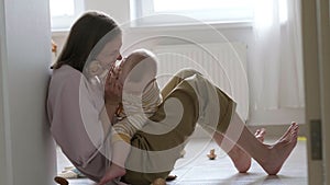 Little baby girl and mommy playing at home sitting on floor. Mother and daughter laughing having fun together