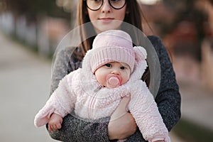 Little baby girl on mother`s hands in pink clothes. Cute baby with peanch colour nipple toy