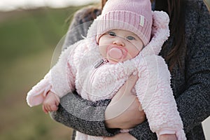 Little baby girl on mother`s hands in pink clothes. Cute baby with peanch colour nipple toy