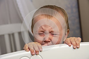 Little baby girl peeks out of the white crib