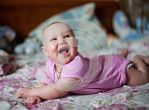 A little baby girl in pink clithes lying at home on the bed