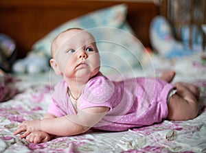 A little baby girl in pink clithes lying at home on the bed