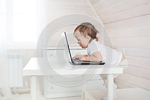 Little baby girl play a laptop on a white table