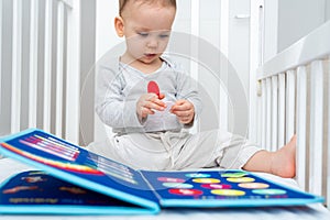 Little baby girl playing with busy book while sitting in crib. Concept of quiet books and modern educational toys