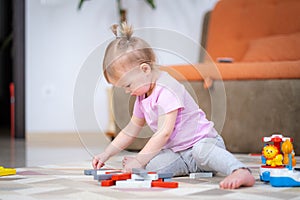 Little baby girl playing color wooden toys at home sitting on floor, early education.