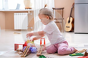 Little baby girl playing color wooden toys at home sitting on floor, early education.