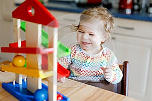 Little baby girl playing with educational toys at home or nursery. Happy healthy toddler child having fun with colorful