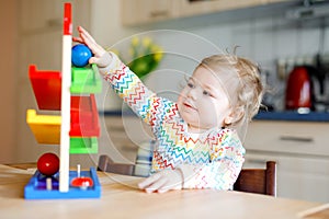 Little baby girl playing with educational toys at home or nursery. Happy healthy toddler child having fun with colorful