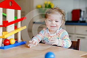 Little baby girl playing with educational toys at home or nursery. Happy healthy toddler child having fun with colorful