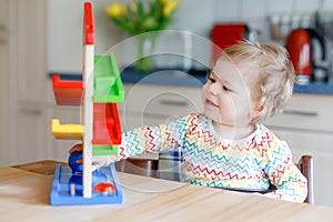 Little baby girl playing with educational toys at home or nursery. Happy healthy toddler child having fun with colorful