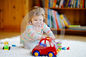 Little baby girl playing with educational wooden toys at home or nursery. Toddler with colorful red car. Child having