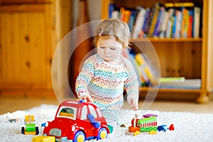 Little baby girl playing with educational wooden toys at home or nursery. Toddler with colorful red car. Child having