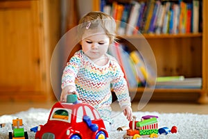 Little baby girl playing with educational wooden toys at home or nursery. Toddler with colorful red car. Child having