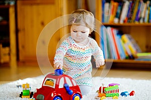 Little baby girl playing with educational wooden toys at home or nursery. Toddler with colorful red car. Child having