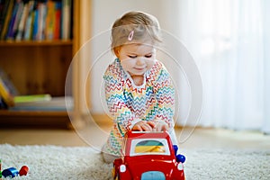 Little baby girl playing with educational wooden toys at home or nursery. Toddler with colorful red car. Child having