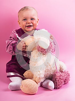 Little baby girl in purple dress with a toy