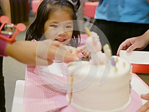 Little baby girl reaching her hand out to a birthday cake in front of her, as it is so irresistibly attracted to her