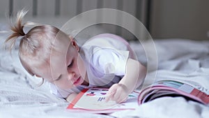 little baby girl reading, looking at pictures in book on bed at home, An inquisitive baby wants to read new fairy tale.