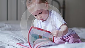 little baby girl reading, looking at pictures in book on bed at home, An inquisitive baby wants to read new fairy tale.