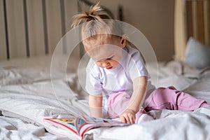 little baby girl reading, looking at pictures in book on bed at home, An inquisitive baby wants to read new fairy tale.