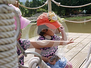 Little baby girl  right , 2 years old, together with her sister, enjoys feeding fishes in the water with dry pallet food