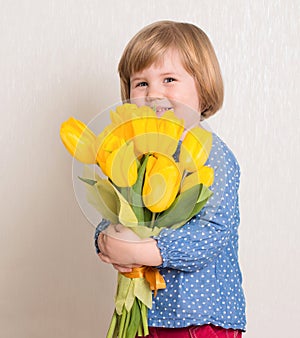 Little baby girl siting on the floor in bright room plays with cat and tulip flowers. Happy child playing at home