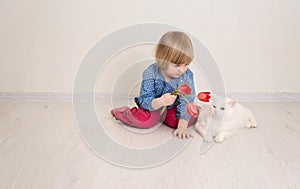 Little baby girl siting on the floor in bright room plays with cat and tulip flowers. Happy child playing at home