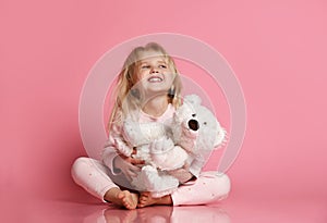 Little baby girl sits on the floor with white teddy bear and smiles happily