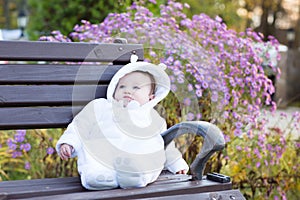 Little baby girl sitting on a bench next to a violet flower bush