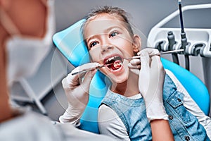 Little baby girl sitting at dental chair with open mouth and feeling fear during oral check up while doctor