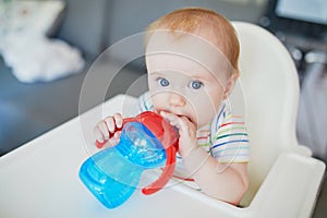 Little baby girl sitting in high chair and drinking water from sippy cup