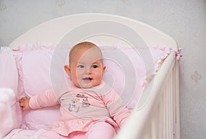 Little baby girl sitting in a pink crib.