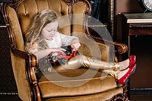 Little baby girl sitting on retro golden chair and playing with red car vintage toy