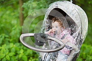 Little baby girl sitting in a stroller under a rain cover