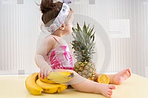 Little baby girl sitting on table with fruits