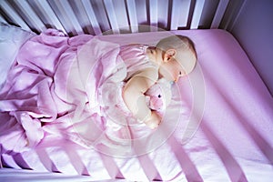 Little baby girl sleep in crib hugging pink bear