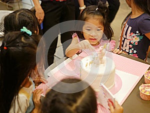 Little baby girl sneakily reaching her hand out to a birthday cake in front of her, as it is so irresistibly attracted to her