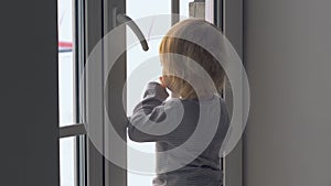 Little baby girl standing near the window and looking outside