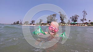 Little baby girl swims in the sea underwater with goggles for swimming