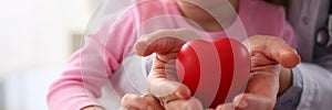 Little baby girl visiting doctor holding in hands red toy heart