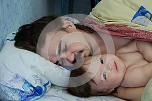 Little baby girl wake up in the morning. Parent tired sleeping. Father lying on bed