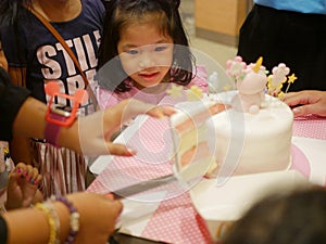 Little baby girl watching a birthday cake in front of her being cut / slices, as it is so irresistibly attracted to her