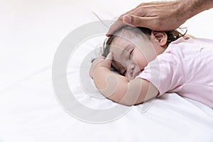 Little baby girl wearing pink cloth sleeping on white bed with hand of daddy on her head calmness at home. Adorable one year old